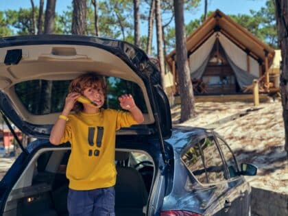 Boy playing with banana in car trunk near glamping tent